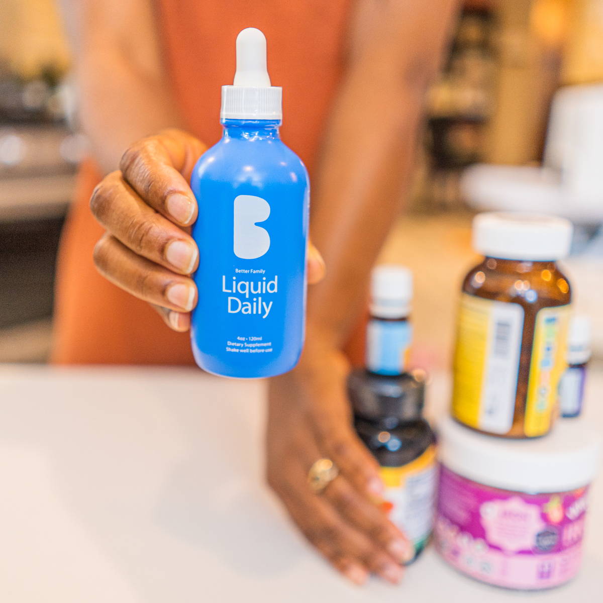 Close-up of a hand holding Better Family Liquid Daily vitamin bottle, emphasizing premium liquid multivitamin for optimal absorption.